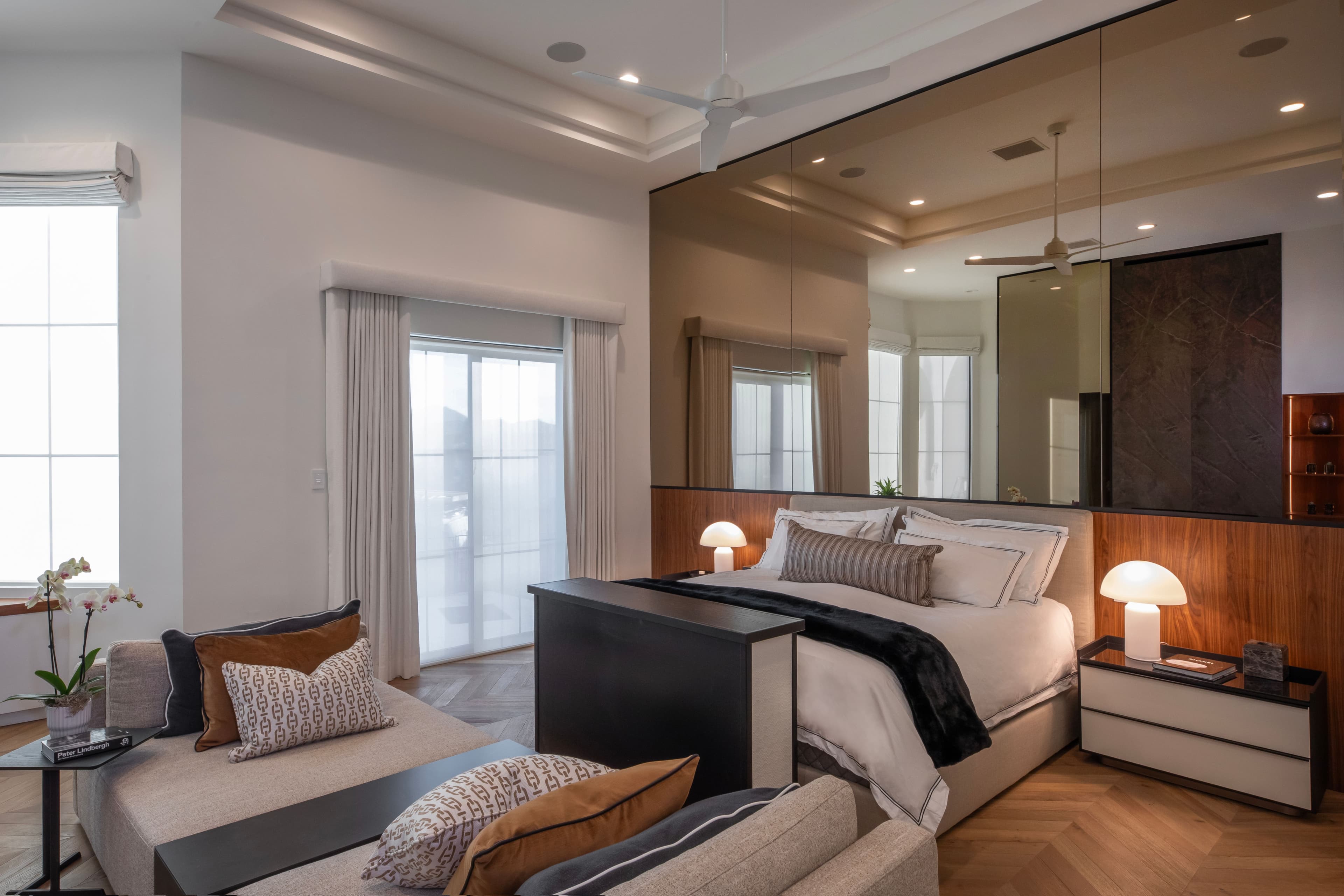 Modern bedroom with a sleek bed, mirrored wall, custom nightstands, and cozy seating area, designed by Febal Casa to showcase expert home remodeling and interior design.